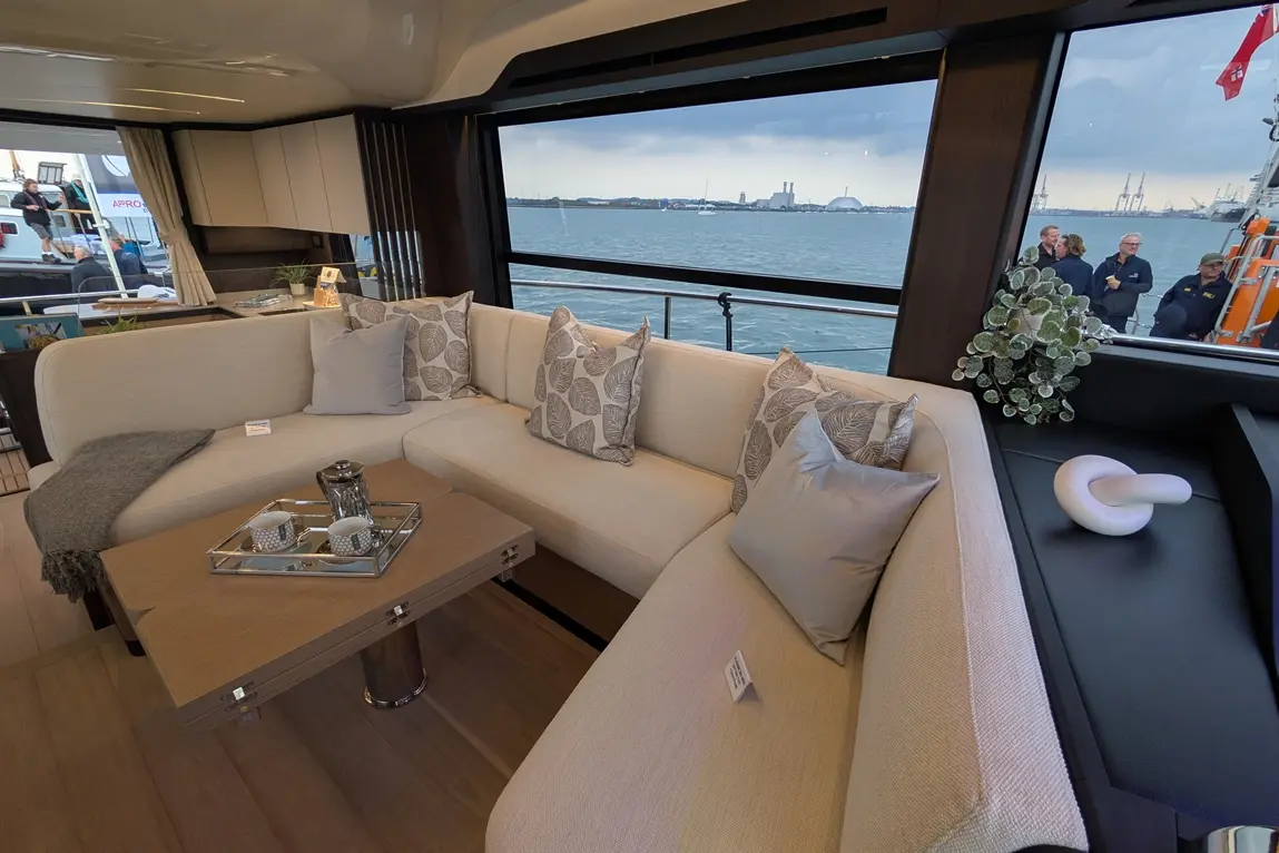 Modern yacht interior featuring a stylish lounge area with cushions, a coffee table, and a scenic waterfront view.